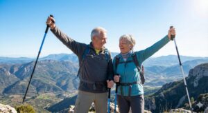 Image 4: An older couple with hiking sticks reaching the top of a hill, looking out at a beautiful landscape.