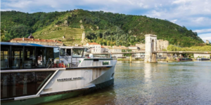 A scenic river cruise ship sailing through a European valley at sunset.