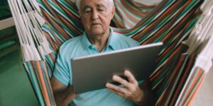 An older adult enjoying an online university course on a laptop in a bright home office.