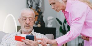 An elderly couple using a digital device together to manage their finances in a bright, comfortable home.