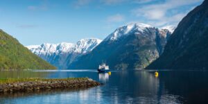 A modern ferry sailing through a serene Scandinavian fjord with majestic mountains in the distance.