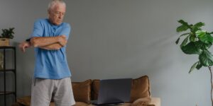 A senior person performing gentle shoulder stretches in a bright, comfortable living room.