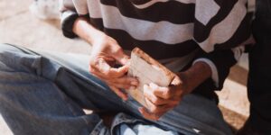 Close up of a senior person's hands carving wood in a sunlit room.