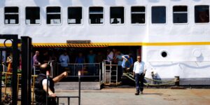 A senior couple disembarking a cruise ship for a port excursion in a sunny coastal city.
