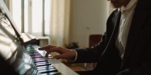 An elderly person's hands on a piano keyboard in a sunlit room.
