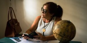 A smartphone, passport, and reading glasses on a table, symbolizing travel preparation.