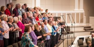A diverse group of seniors singing together in a bright community hall.