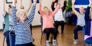 A senior adult performing gentle shoulder mobility exercises in a comfortable home environment.