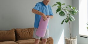 A senior person stretching their wrists in a cozy, sunlit room.