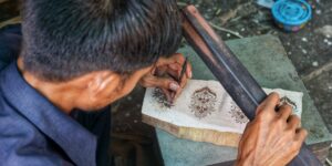 An elderly person carving a block printing design at a well-lit craft station.