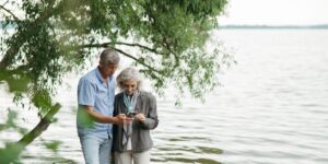 A senior traveler looking at a smartphone at a scenic mountain train station.