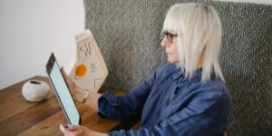 An elderly person reading on a tablet in a modern, sunlit library.