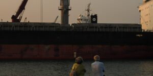 A senior couple enjoying the view of a port city from a cruise ship deck.