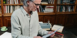 An elderly person reading a vintage recipe book in a sunlit kitchen.