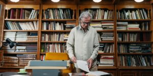 A senior adult conducting historical research in a library with a map and magnifying glass.