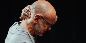 An older adult performing a gentle neck stretch while seated at a desk.