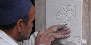 An elderly person carving a design into a linoleum block for printing.