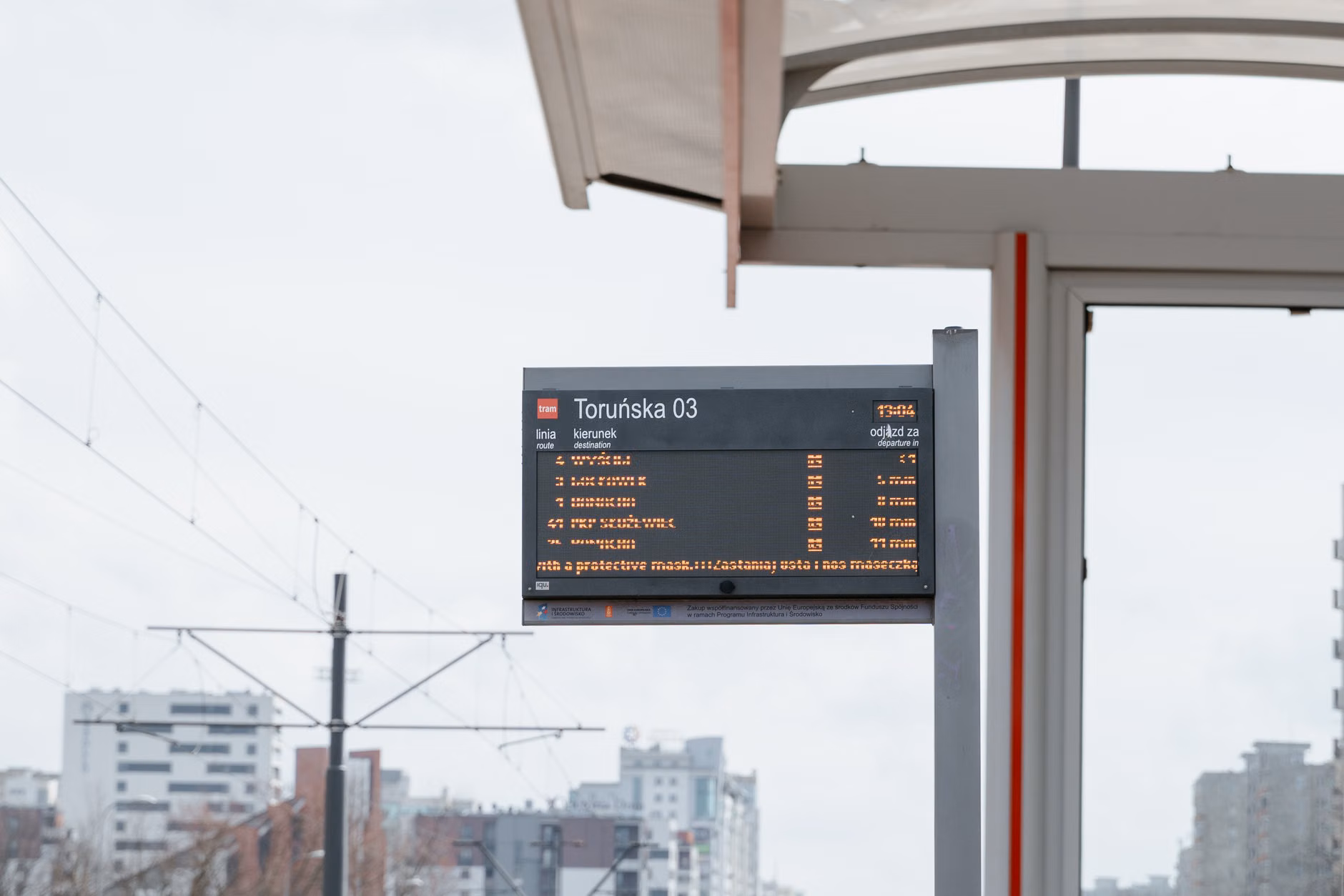 A senior person checking a digital transit information display at a bus stop.