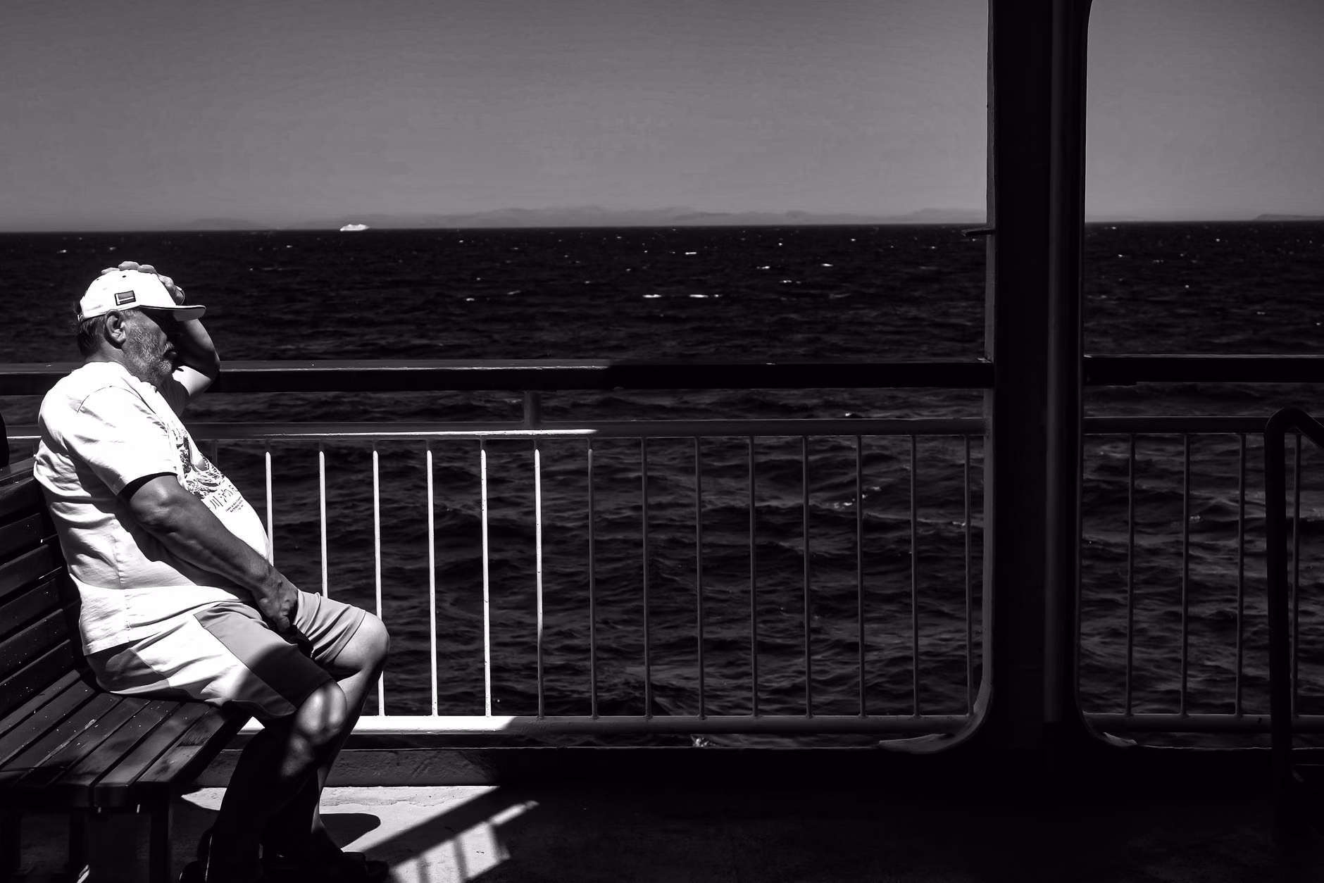 Senior traveler resting on an ergonomic bench with armrests at a coastal viewpoint.