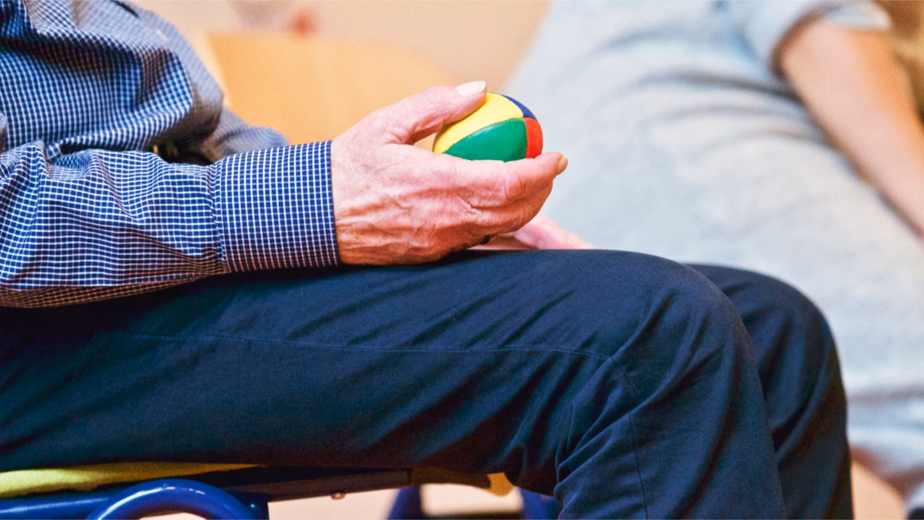 A senior adult sitting in a chair practicing hand-squeeze exercises with good posture.
