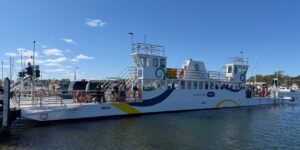 A modern passenger ferry docking at a scenic island port under a clear blue sky.