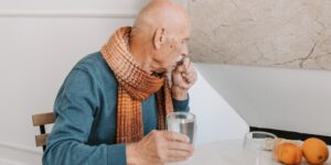 A senior person sitting at a table with water and fruit, promoting healthy hydration habits.
