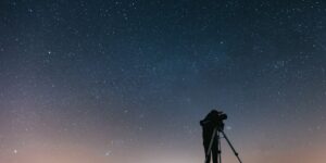 A senior adult observing the night sky with a telescope in a tranquil setting.