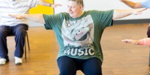 An older adult performing seated arm circles in a comfortable home setting.