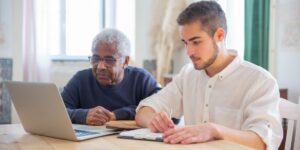 A young mentor and a senior adult collaborating on a digital device in a community space.