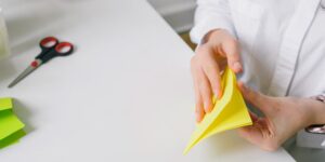 Hands carefully folding colorful origami paper in a well-lit room.