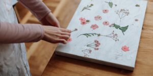 Close-up of hands arranging pressed flowers on a wooden table.