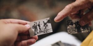 Hands holding an old family photo next to a digital tablet showing a family tree.