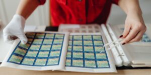 Hands using stamp tweezers to organize a stamp collection on a desk.