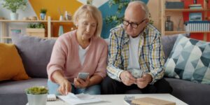 An older couple using a tablet to manage their finances in a sunlit room.
