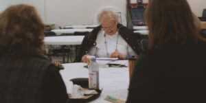 A group of older adults gathered around a table with historical recipes and ingredients, fostering community through culinary history.