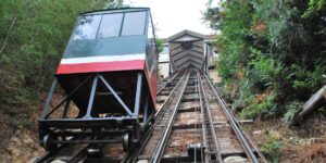 A scenic view of a vintage funicular climbing a steep hill toward an ancient European city.