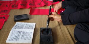An older adult practicing the art of calligraphy at a sunlit desk.