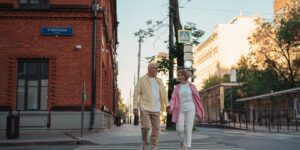 An active senior couple walking through a sunny city square with lightweight daypacks.