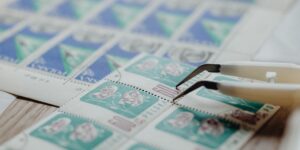 Hands carefully using tweezers to handle a vintage stamp for a collection.