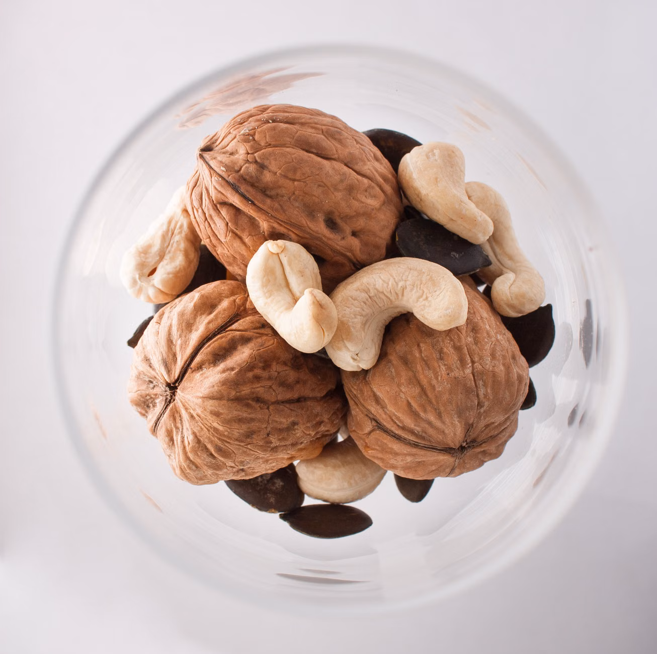 Vitamin E for Longevity: Practical Dietary Strategies for Skin and Cellular Health 2 A selection of healthy nuts and seeds in glass bowls, rich in Vitamin E.