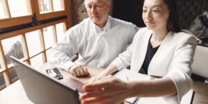 An older adult and a young professional collaborating on a digital project in a bright office.