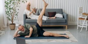 An active senior performing seated hip mobility exercises in a bright, comfortable living room.