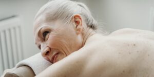 An older adult performing a gentle shoulder roll while seated in a comfortable home environment.