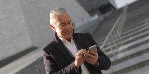 An older adult using a smartphone at a modern bus stop to navigate transit routes.