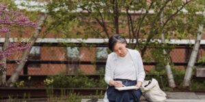 An older adult enjoying a quiet moment of bird-sketching in a lush garden.