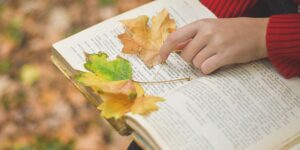 Senior hands pressing an autumn leaf in a book.