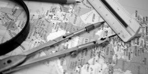 Hands using a compass and pencil to draw a map on a wooden desk.