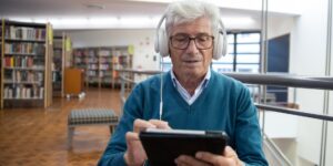 An older adult using a tablet in a modern library setting, reflecting digital accessibility.