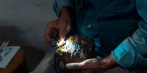 An elderly person examining a mineral specimen with a magnifying glass.