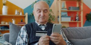 A senior adult safely managing digital banking on a smartphone in a bright home environment.